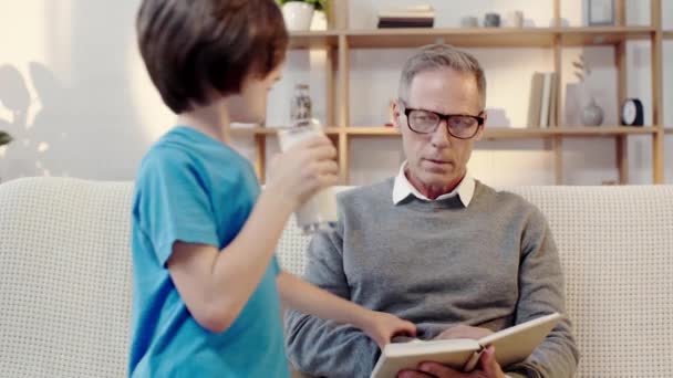 Χαρούμενος Παππούς Διαβάζοντας Βιβλίο Αγκαλιάζοντας Τον Εγγονό Που Πίνουν Γάλα — Αρχείο Βίντεο