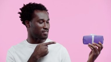 Pozitif Afrikalı Amerikalı bir adam hediye paketini sunuyor. Pembe üzerinde izole edilmiş.