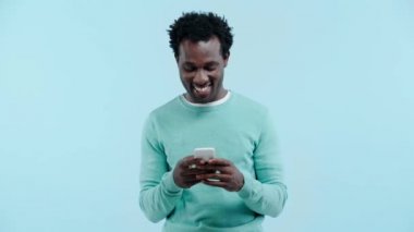 Gülümseyen Afrikalı Amerikalı adam mavi hattan izole edilmiş akıllı telefon kullanıyor.