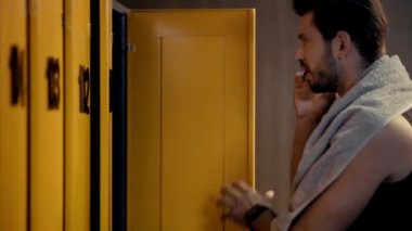 Yakışıklı sporcu dolapların yanında akıllı telefondan konuşuyor. 