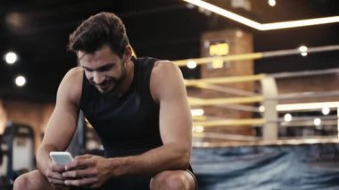 Spor salonunda akıllı telefon kullanan neşeli sporcu.