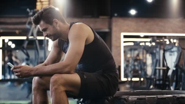 Χαρούμενος Αθλητής Χρησιμοποιώντας Smartphone Στο Γυμναστήριο — Αρχείο Βίντεο