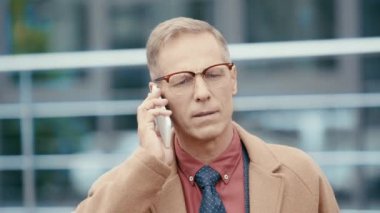 Paltoyla gülümseyen iş adamı akıllı telefondan konuşuyor. 