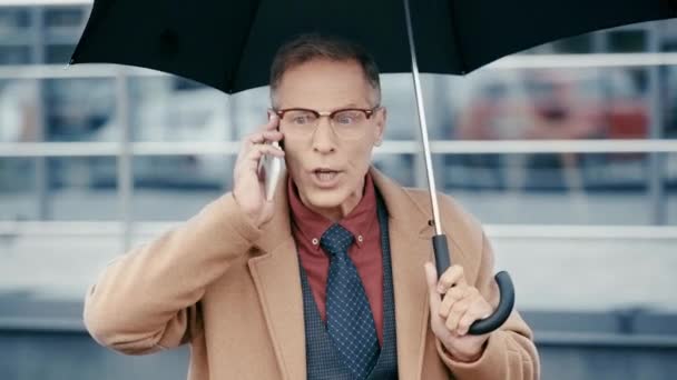 Wütender Geschäftsmann Hält Regenschirm Der Hand Und Spricht Auf Smartphone — Stockvideo
