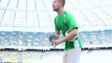 Futbolcu topu tutuyor, yürüyor ve su içiyor. 