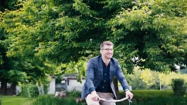 一个戴眼镜 骑自行车在树旁挥手的快乐男人 — 图库视频影像
