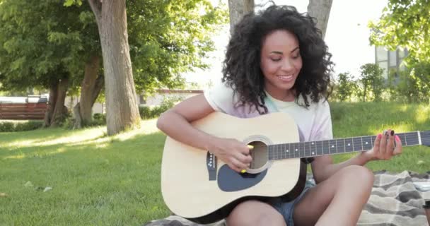 Χαμογελώντας Αφροαμερικανή Γυναίκα Παίζει Ακουστική Κιθάρα Καρό Στο Πάρκο — Αρχείο Βίντεο