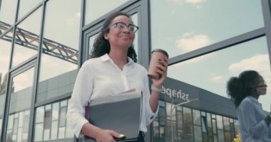 Gülümseyen Afro-Amerikan iş kadını elinde kağıtlar ve kağıt bardakla Kentsel caddede