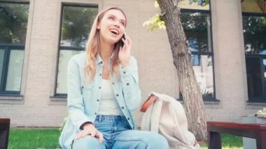 Sırt çantasının yanında akıllı telefondan konuşan gülümseyen bir öğrenci. 