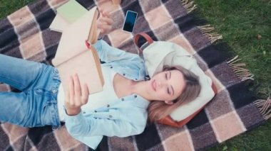 Parkta ekose kitap okuyan gülümseyen öğrenci manzarası 