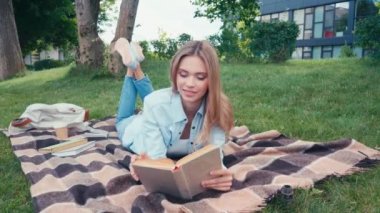 Parkta ekose üzerinde yatarken pozitif öğrenci kitabı okuyor. 