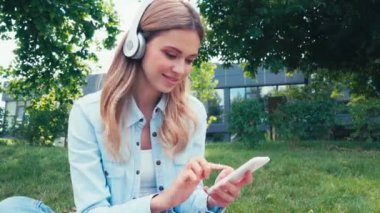 Parkta akıllı telefon ve kulaklık kullanan pozitif öğrenci 