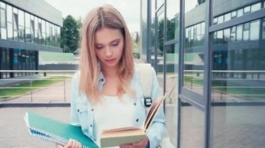 Şehir caddesinde yürürken defter okuyan öğrenci 