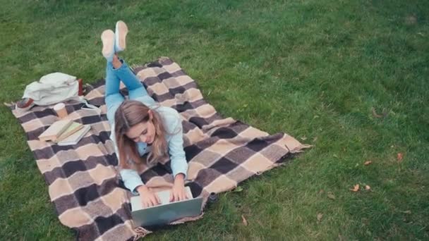 パーク内の毛布にノートパソコンを使用した笑顔の学生の概要 — ストック動画
