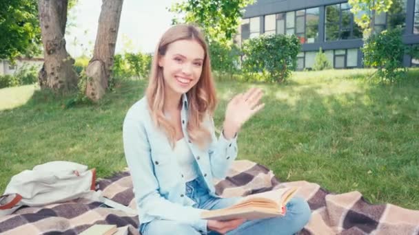 Estudante Sorrindo Acenando Mão Para Câmera Enquanto Lia Livro Sobre — Vídeo de Stock