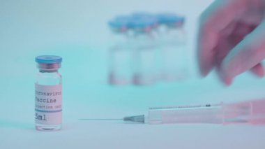 Şırıngayı şişenin yanında mavi üzerine aşı harfleriyle alan kişinin kırpılmış görüntüsü.