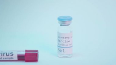 Kan örneğiyle test tüpü ve mavi üzerinde koronavirüs aşısı olan bir şişe.