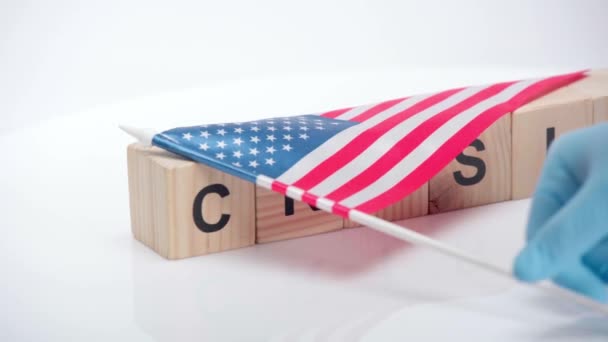 白い表面に危機の言葉を持つブロックからアメリカの旗を取る人 — ストック動画