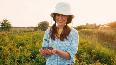 Şapkadaki kadın elinde küçük bir bitkiyle toprağı tutuyor.