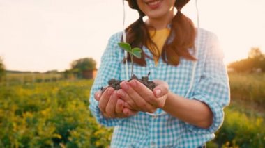 Elinde küçük bir bitkiyle toprağı tutan kadın manzarası.