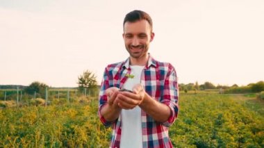 Heyecanlı sakallı adam konuşuyor ve elinde küçük bir bitkiyle toprağı tutuyor.