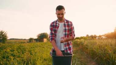 Ekose gömlekli çiftçinin elinde kova ve tarlaya tohum ekmesi yavaş çekimde. 