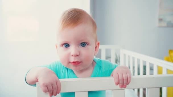 赤ちゃんのベビーベッドに立って家でカメラを見て — ストック動画