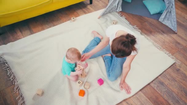 幼児の息子の近くに座っておもちゃで遊んでいる裸足の母親のトップビュー — ストック動画