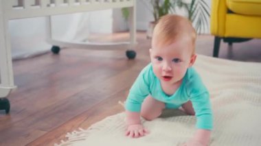 Çocuk evde emeklerken kameraya bakıyor.