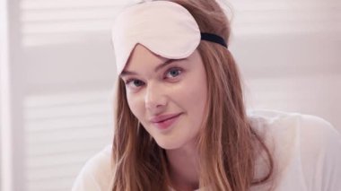 Başında uyku maskesi olan genç bir kadın kameraya bakıyor.