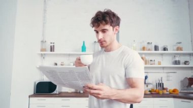 Genç adam mutfakta kahve içerken gazete okuyor. 