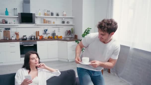 Hombre Dando Café Besar Mujer Sexy Con Teléfono Inteligente Sofá — Vídeo de stock