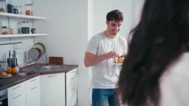 Mann mit Pfannkuchen füttert sinnliche Frau mit Smartphone in Küche 