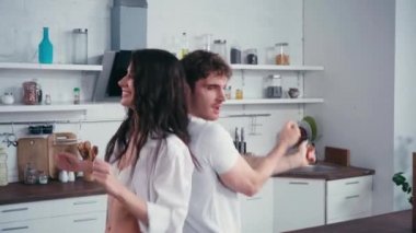 Erkek arkadaşının yanında dans eden seksi kadın, mutfak masasında meyve ve akıllı telefon. 