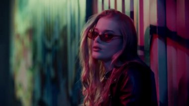 Güneş gözlüklü şık bir kadın duvarın yanındaki duvara grafiti ile bakıyor. 