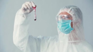 Tehlikeli madde giysisi içindeki bilim adamının seçici odak noktası gri üzerinde test tüpü tutuyor.