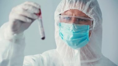 Gri üzerinde test tüpü tutan tehlikeli madde kostümlü bilim adamının odak noktası.