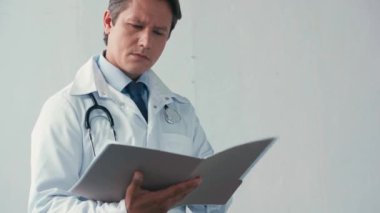 Beyaz önlüklü ciddi bir doktor gri dosyaya bakıyor.