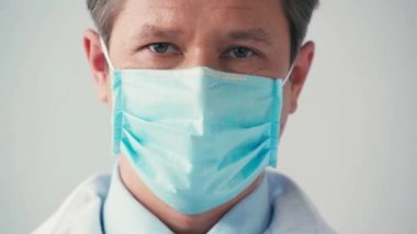 Tıbbi maske takmış bir doktor Grey 'in kamerasına bakıyor.