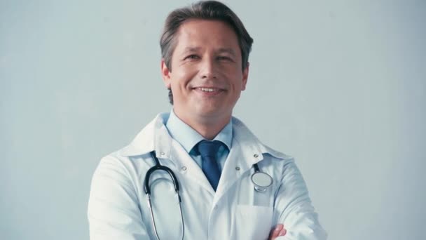 Arzt in weißem Mantel mit Stethoskop blickt in Kamera auf grau