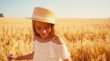 Beyaz elbiseli ve hasır şapkalı kız buğday tarlasına bakıyor. 