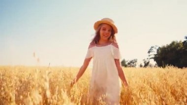 Beyaz elbiseli ve hasır şapkalı neşeli kız buğday tarlasında yürüyor. 