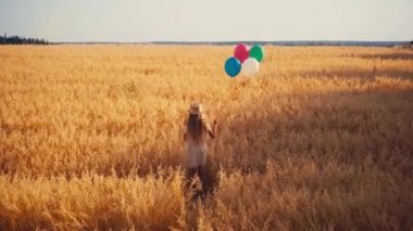 Buğday tarlasında balonlarla yürüyen beyaz elbiseli bir kız.