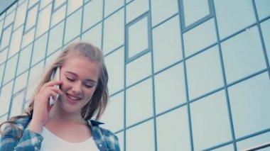 Düşük açılı, cam cepheli, akıllı telefondan konuşan bir kadın.