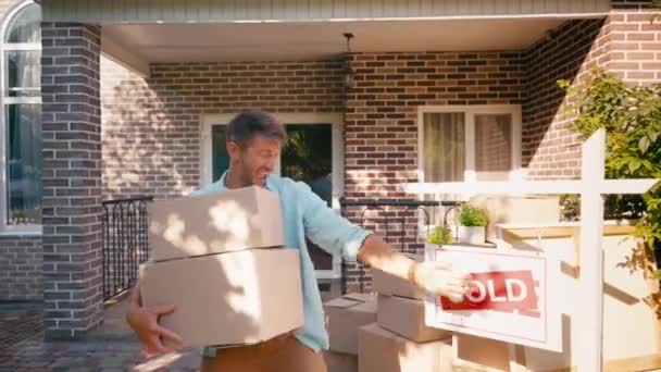 Man pointing with hand at sold board, holding boxes and jumping near new house — Stock Footage Man Pointing Hand Sold Board Holding Boxes Jumping New House Stock Footage