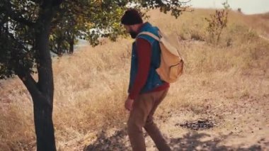 Sırt çantalı turist aşağı inip ağaca yaslanıyor.
