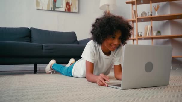 Sorrindo Menina Americana Africana Deitada Tapete Olhando Para Laptop Casa — Vídeo de Stock