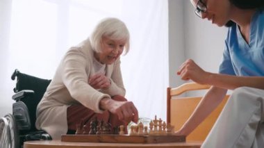 Genç hemşire yaşlı kadınla satranç oynarken hiçbir işaret göstermiyor.