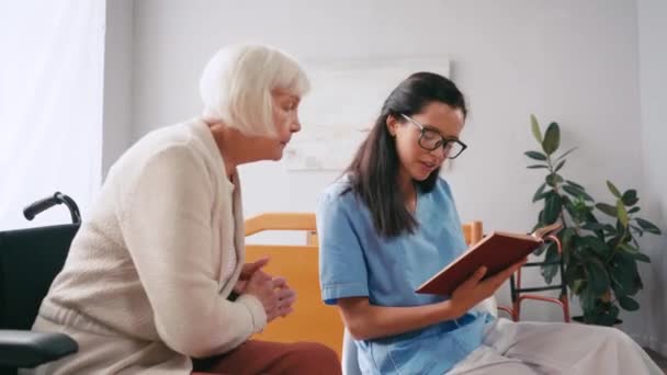 若いブルネットの看護師が老人ホームで本を読む — ストック動画