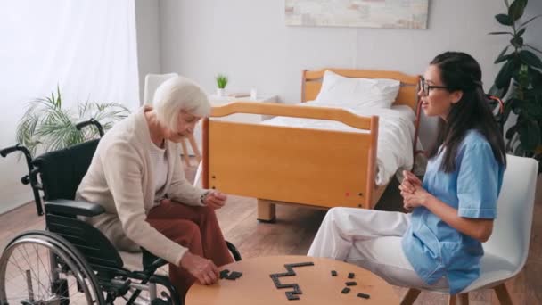 Senior Femme Fauteuil Roulant Jouer Dominos Avec Jeune Infirmière — Video